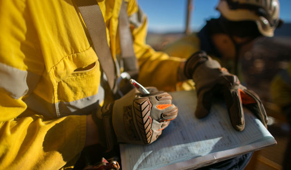 A man wearing yellow construction safety compliant gear holds a clipboard, indicating his role in a work-related environment.