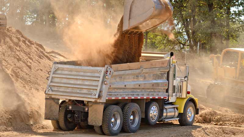 A profile view of a dump truck, in a construction setting, that has DOT-compliant red and white reflective tape.