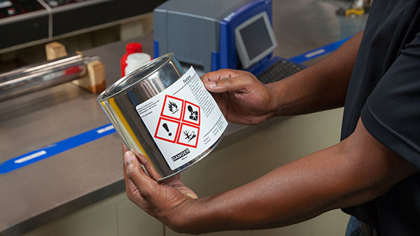 An up-close image of a worker applying a GHS label to a secondary container.