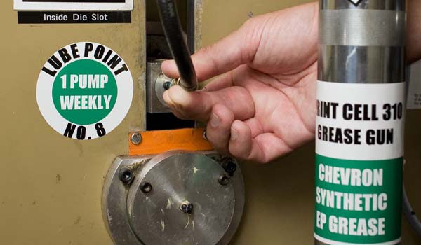 A worker using a properly labeled grease gun, that meets industry standards, to lube an area of the manufacturing line.